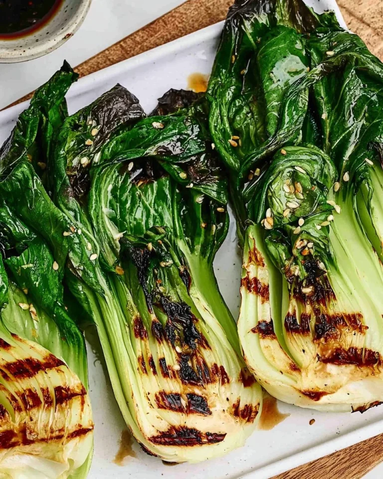 Grilled bok choy served on a plate with sesame seeds and garnishes.